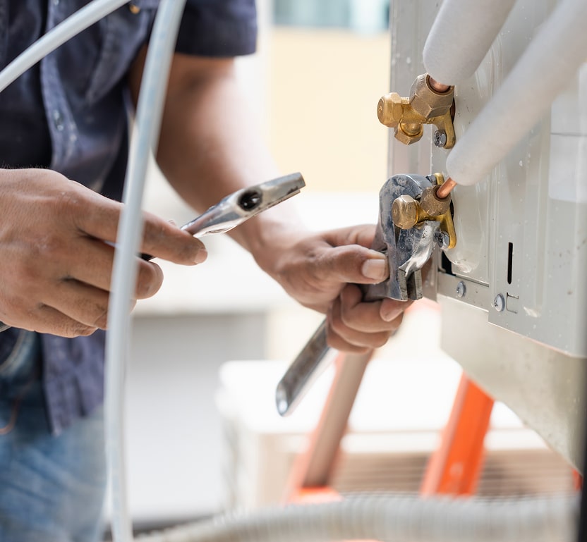 a worker using some tools on an AC unit performing maintenance.