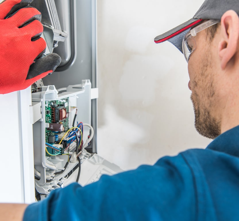 A worker inspecting the electrical panel of a furnace unit