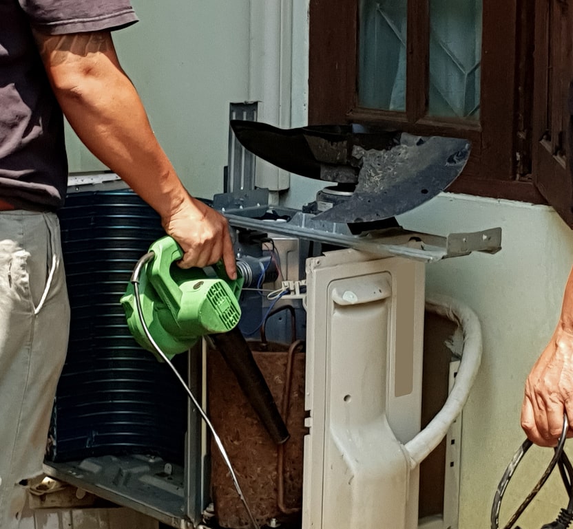 a worker using a blower on some AC parts