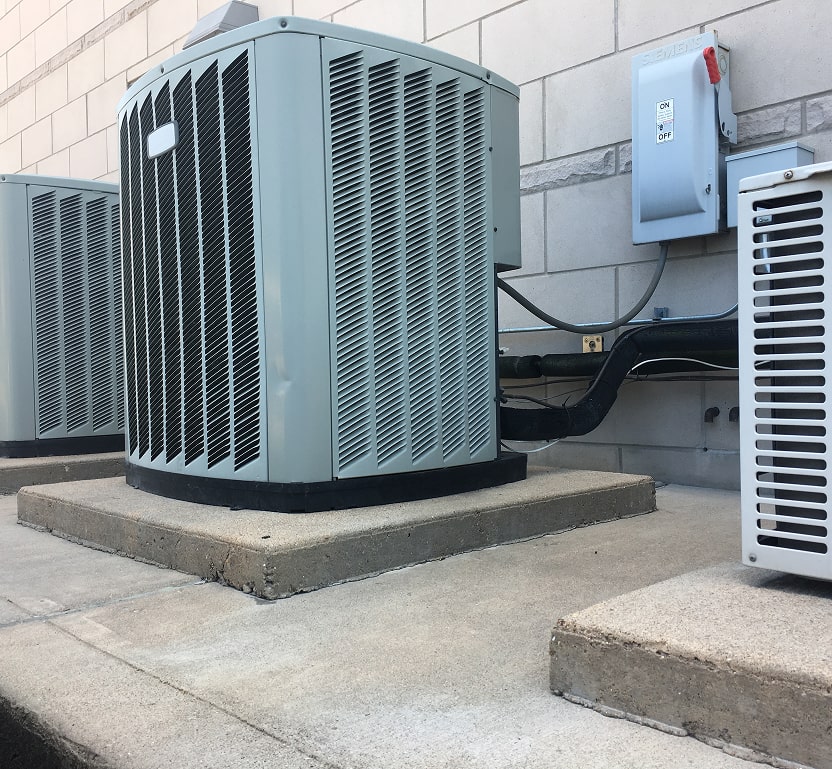 2 outdoor units seen near an electrical shutoff near a building.